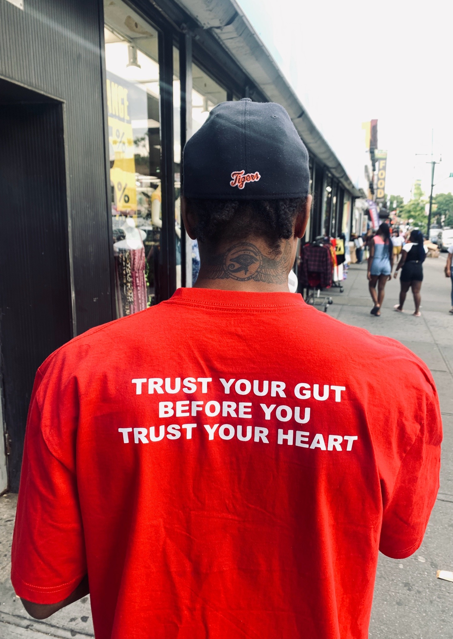 A Black man in a red t-shirt. The slogan on the back says "trust your gut before you trust your heart" in white and all caps.